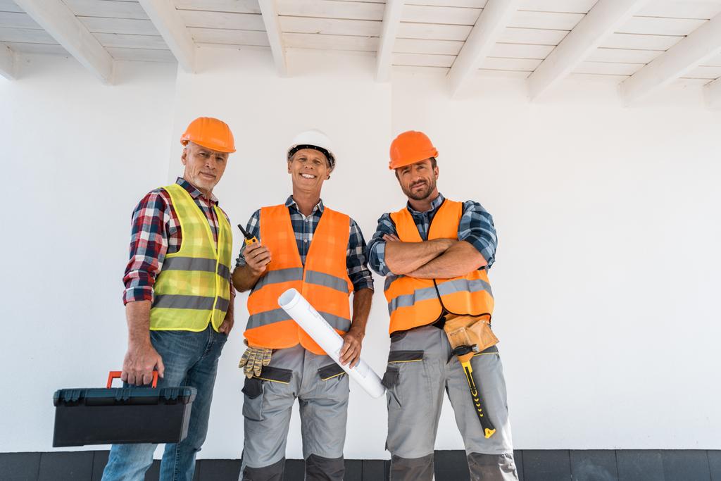 gelukkige constructeurs staan met blauwdruk en gereedschapskist  - Foto, afbeelding