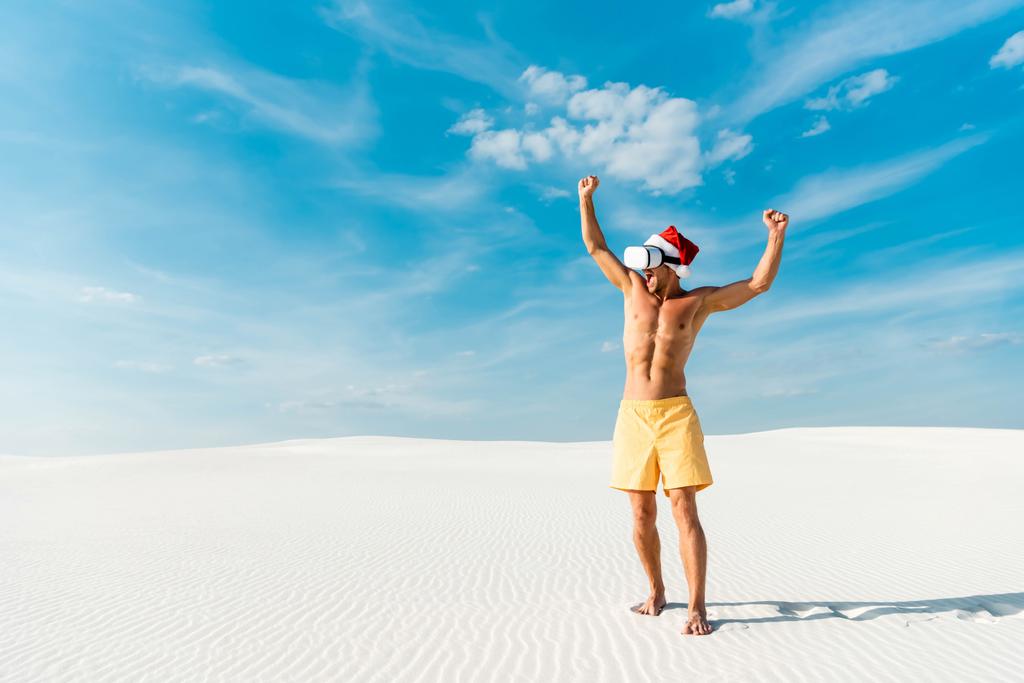 Сексуальний чоловік у Санта-капелюсі з заголовком віртуальної реальності, що показує "так" жест на пляжі Мальдівів.  - Фото, зображення