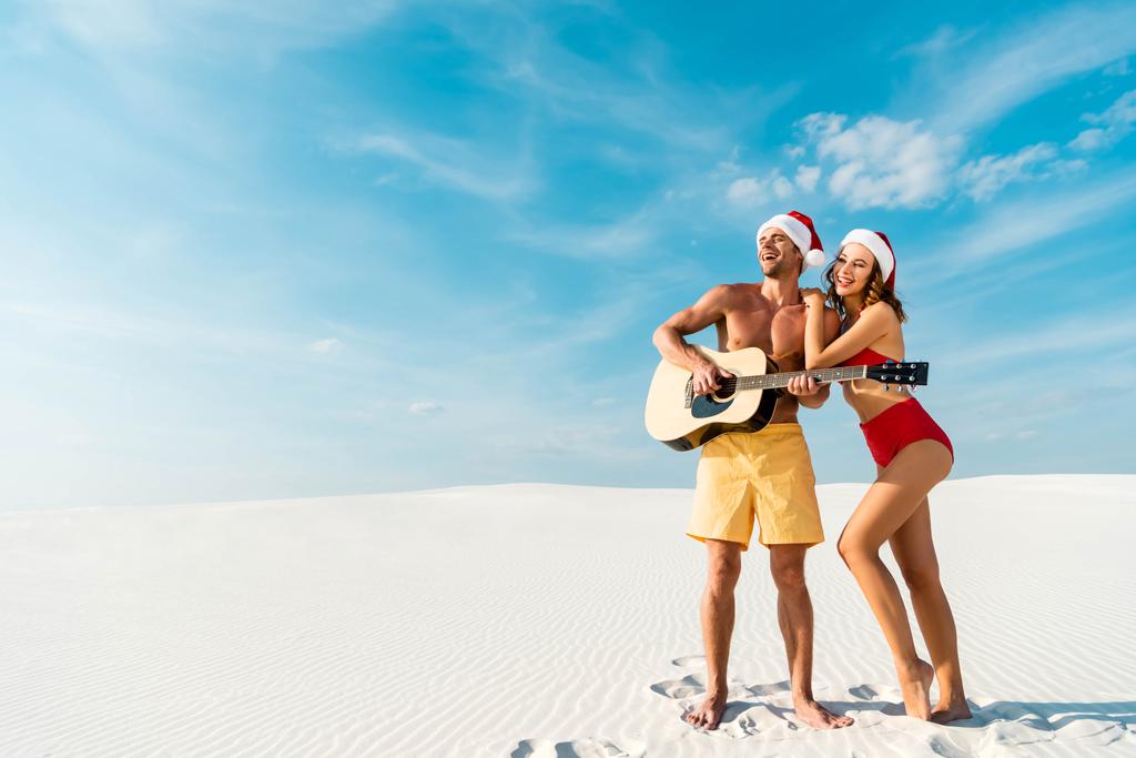 セクシーな彼女とボーイフレンドのパノラマショットは、モルディブのビーチでアコースティックギターを演奏  - 写真・画像