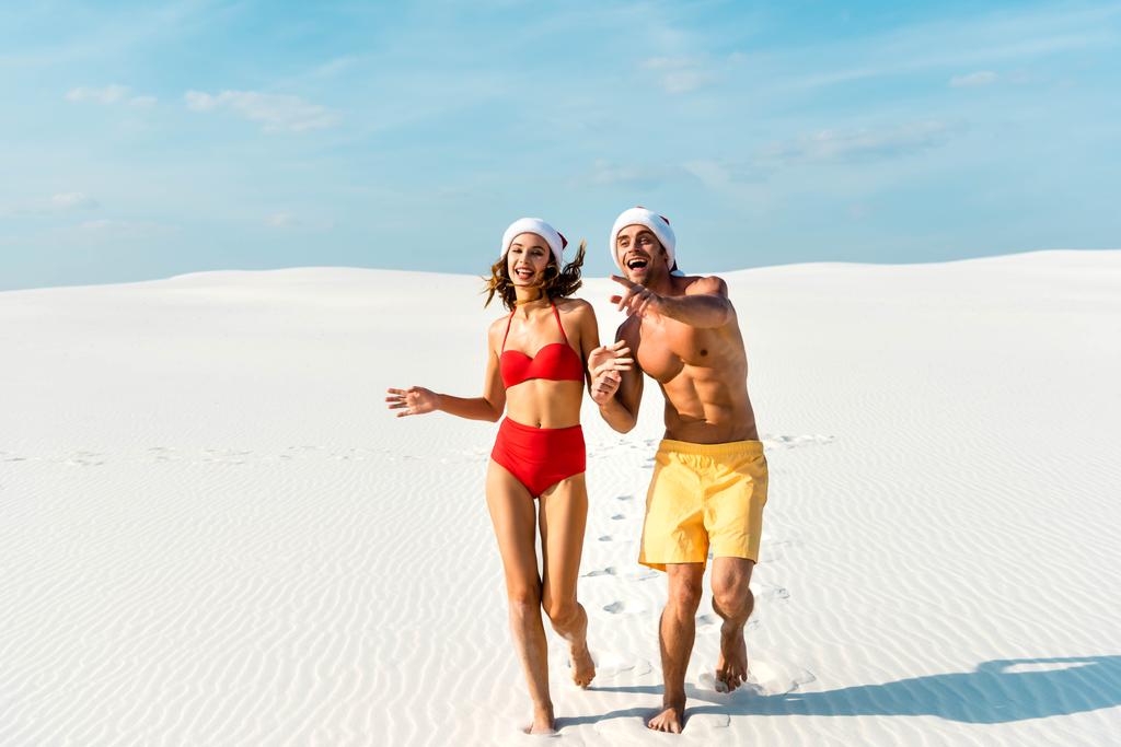セクシーガールフレンドとボーイフレンドでサンタ帽子でランニングとポインティング指でビーチでモルディブ  - 写真・画像
