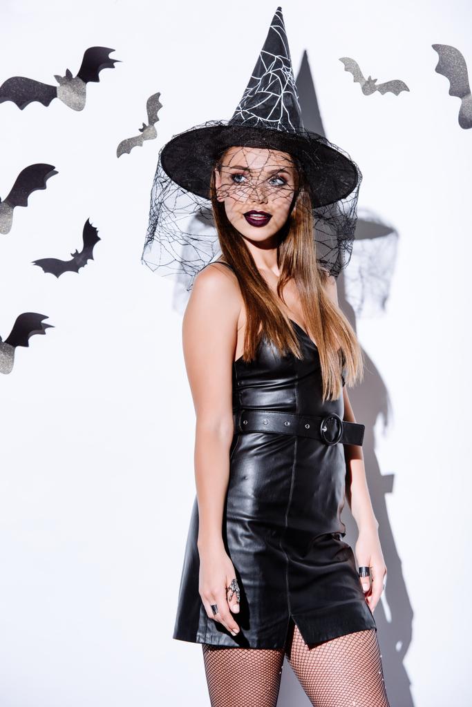 girl in black witch Halloween costume near white wall with decorative bats - Photo, Image