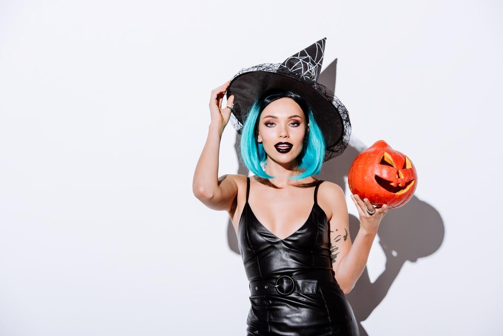 sexy girl in black witch Halloween costume with blue hair holding spooky carved pumpkin on white background - 写真・画像