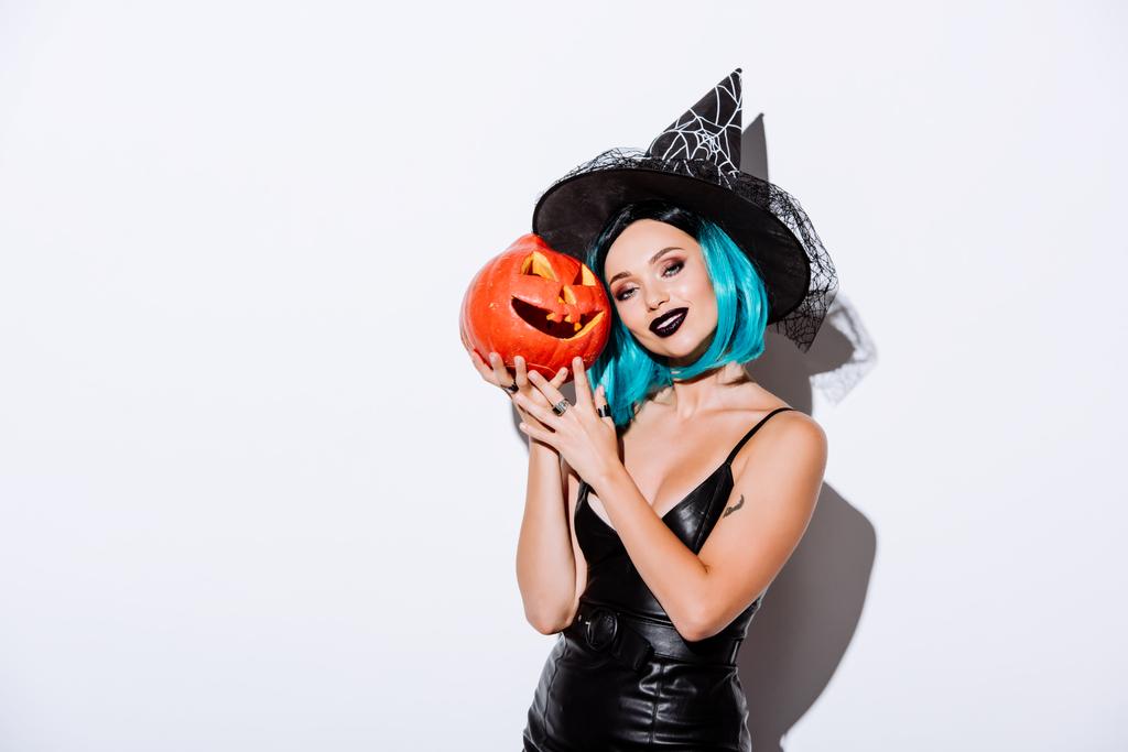 sexy dziewczyna w czarny czarownica Halloween kostium z niebieskimi włosami gospodarstwa straszne rzeźbione dyni na białym tle - Zdjęcie, obraz