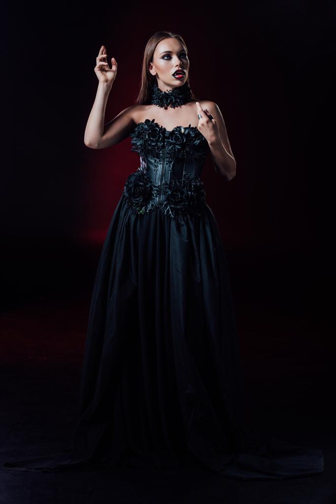 asustadiza chica vampiro con colmillos en vestido gótico negro sobre fondo negro
 - Foto, imagen