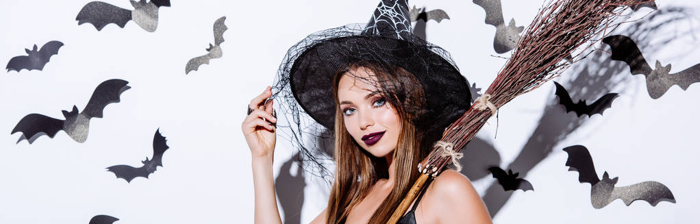 panoramic shot of girl in black witch Halloween costume with broom near white wall with decorative bats - Photo, Image