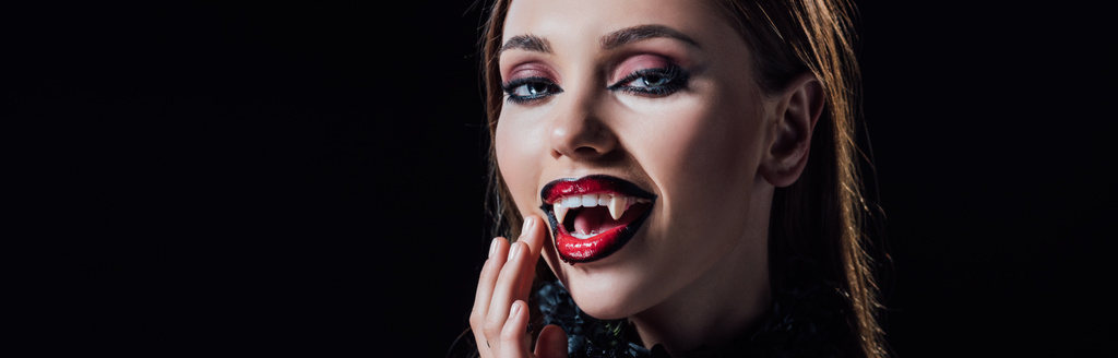 plano panorámico de chica vampiro miedo mostrando colmillos en vestido gótico negro aislado en negro
 - Foto, Imagen