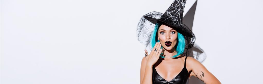 tiro panorâmico de menina chocada em preto bruxa traje de Halloween com cabelo azul no fundo branco
 - Foto, Imagem