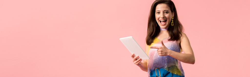 plano panorámico de excitado joven y elegante chica disco apuntando con el dedo a la tableta digital aislado en rosa
 - Foto, Imagen