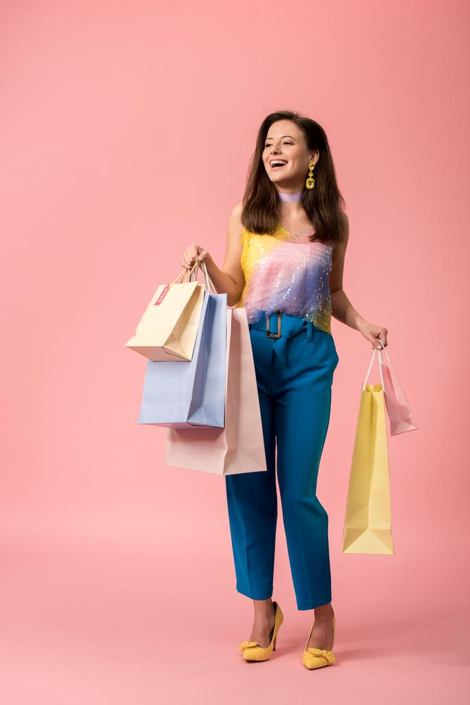 volledige weergave van gelukkig stijlvol disco meisje met boodschappentassen op roze - Foto, afbeelding