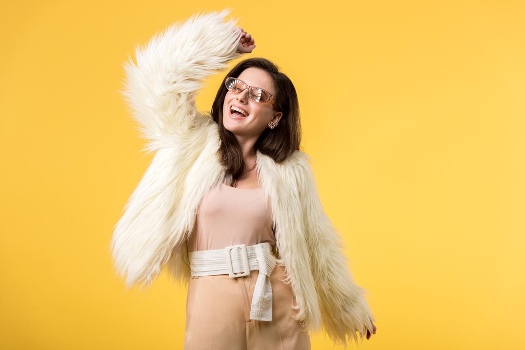 excited party girl in faux fur jacket and sunglasses dancing isolated on yellow - Photo, Image