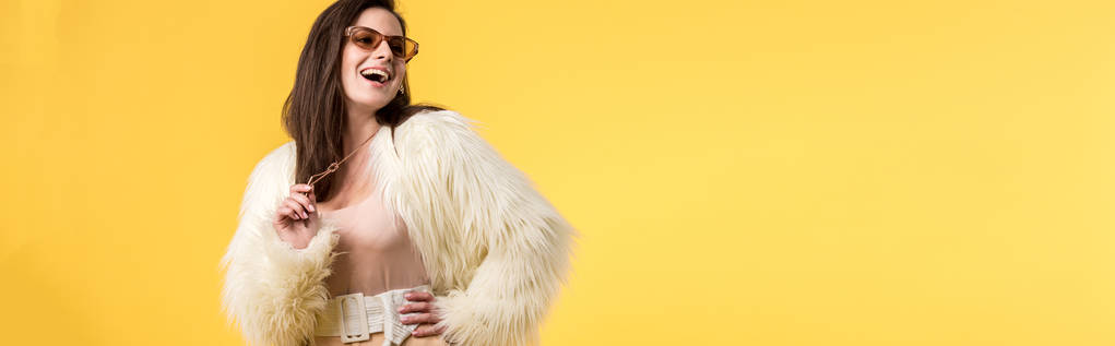 panoráma felvétel izgatott party lány faux szőrme kabát és napszemüveg elszigetelt sárga - Fotó, kép