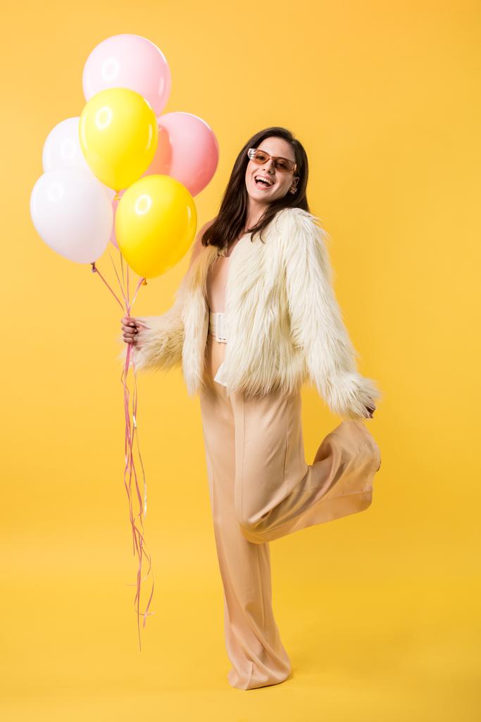 счастливая тусовщица в искусственном меховом пиджаке и солнцезащитных очках, позирующих с воздушными шарами
 - Фото, изображение
