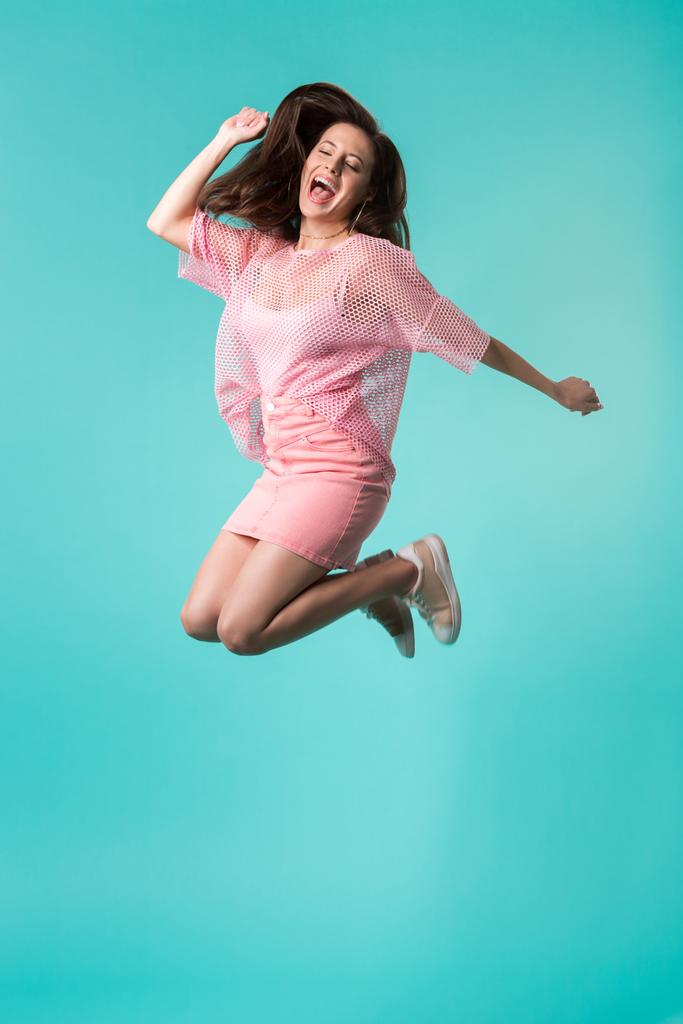 menina animado com a boca aberta em roupa rosa pulando isolado em turquesa
 - Foto, Imagem