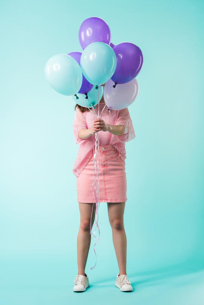 дівчина в рожевому вбранні тримає повітряні кулі перед обличчям на бірюзовому фоні
 - Фото, зображення