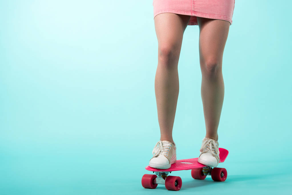 cropped view of girl in pink outfit standing on penny board on turquoise background - Photo, Image