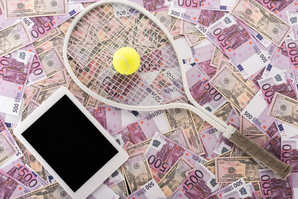 ユーロ紙幣とドル紙幣の上に空白の画面、テニスラケットとボール、スポーツ賭博の概念を持つデジタルタブレットのトップビュー - 写真・画像