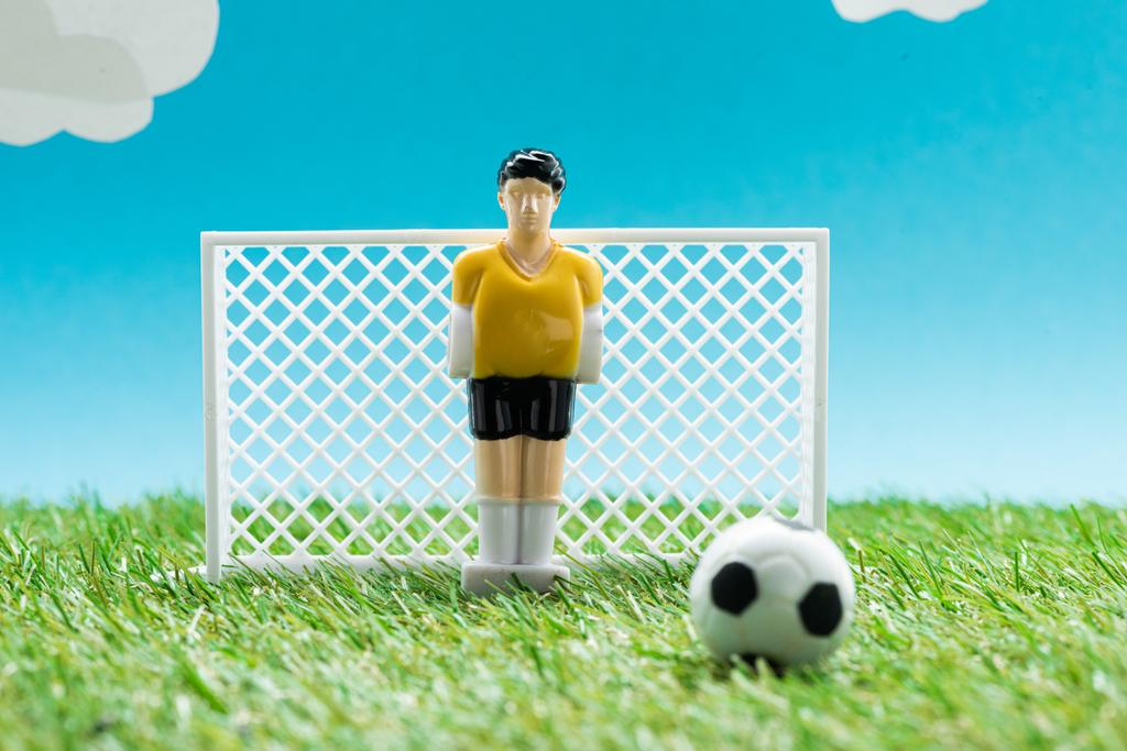 hračka brankář v blízkosti miniaturní fotbalové brány a míč na modrém pozadí s mraky, sportovní sázení koncept - Fotografie, Obrázek