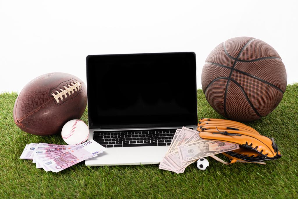laptop perto de bolas esportivas, luva de beisebol, notas de euro e dólar em grama verde isolada em branco, conceito de apostas esportivas
 - Foto, Imagem