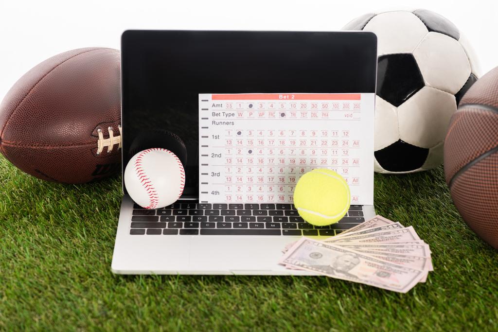 notebook v blízkosti sportovních míčků a sázkových listů na zelené trávě izolované na bílé, koncept sportovního sázení - Fotografie, Obrázek