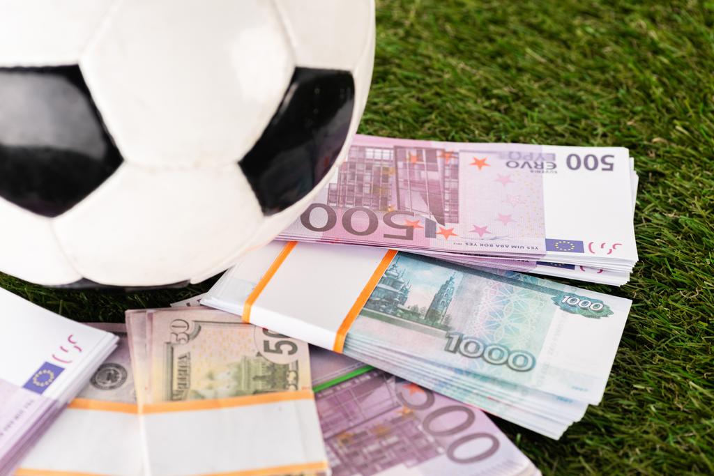επιλεκτική εστίαση των πακέτων τραπεζογραμματίων ευρώ και δολαρίου κοντά στην μπάλα ποδοσφαίρου στο πράσινο γρασίδι, έννοια αθλητικών στοιχημάτων - Φωτογραφία, εικόνα