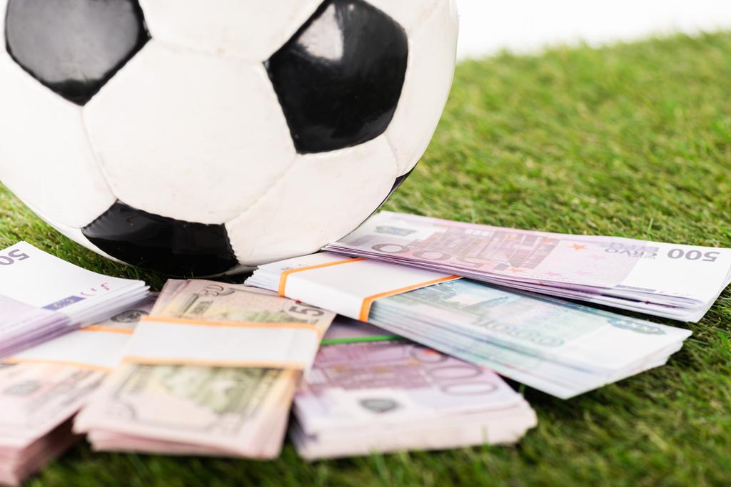 selectieve focus van euro- en dollarbankbiljetten in de buurt van voetbal op groen gras, geïsoleerd op wit, sportweddenschappen - Foto, afbeelding