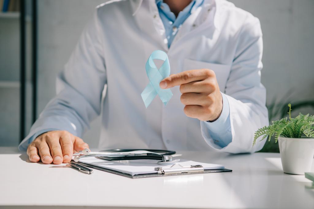 cropped view of doctor sitting at desk and showing blue awareness ribbon - Photo, Image