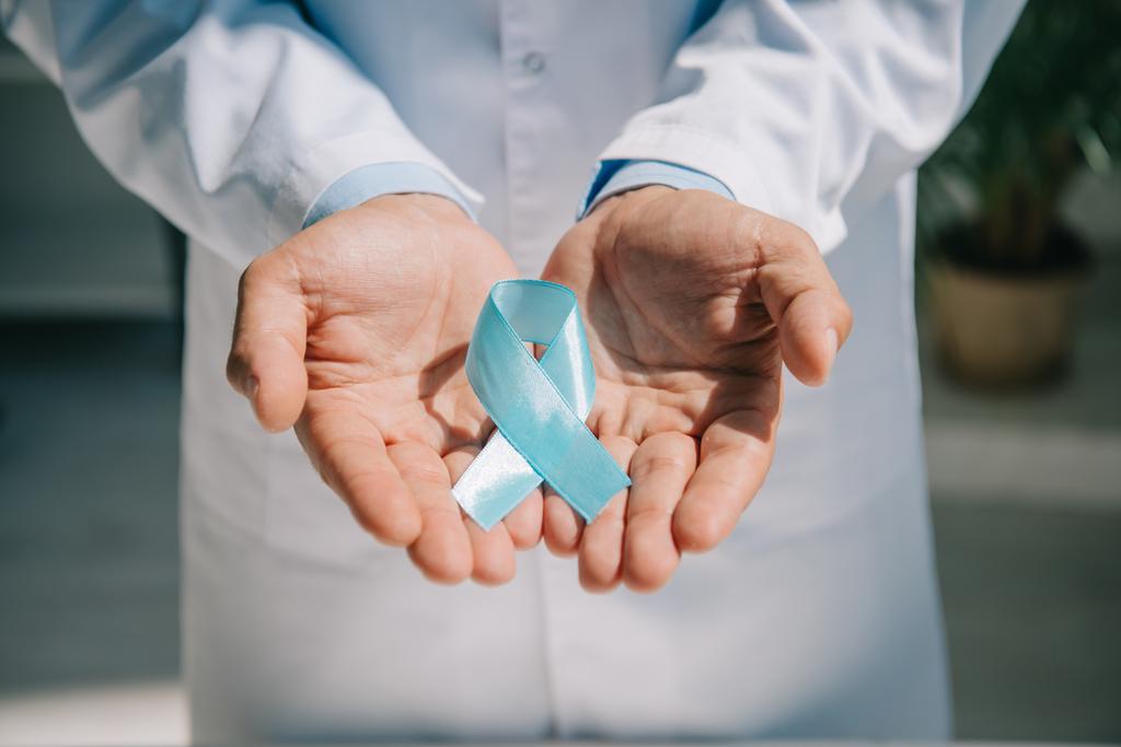 bijgesneden weergave van arts in witte jas met blauw bewustzijnslint - Foto, afbeelding
