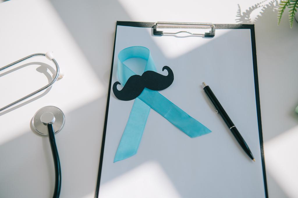 cinta de conciencia azul, bigote cortado en papel y pluma en el portapapeles con papel en blanco cerca del estetoscopio
 - Foto, imagen