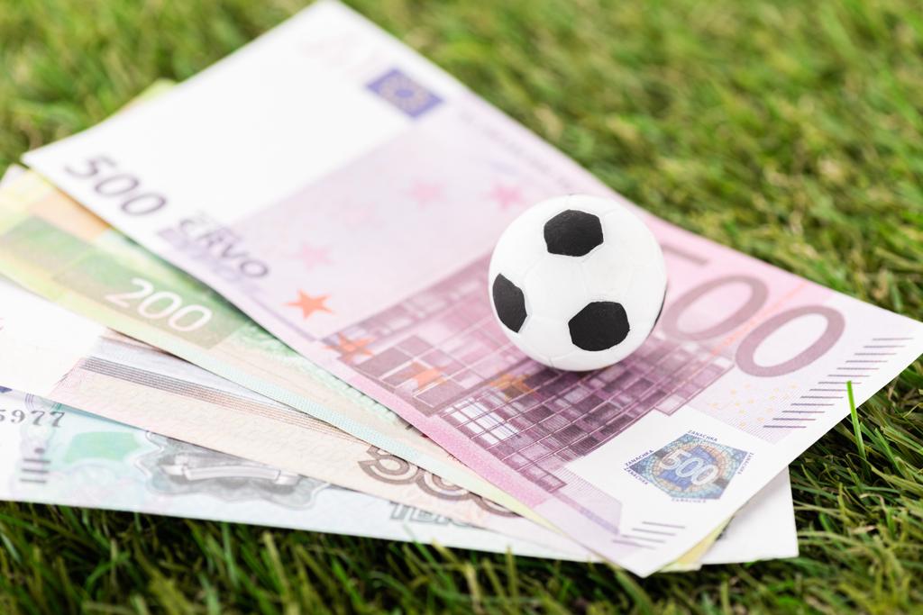 селективный фокус игрушечного футбольного мяча и банкнот евро на зеленой траве, концепция ставок на спорт
 - Фото, изображение
