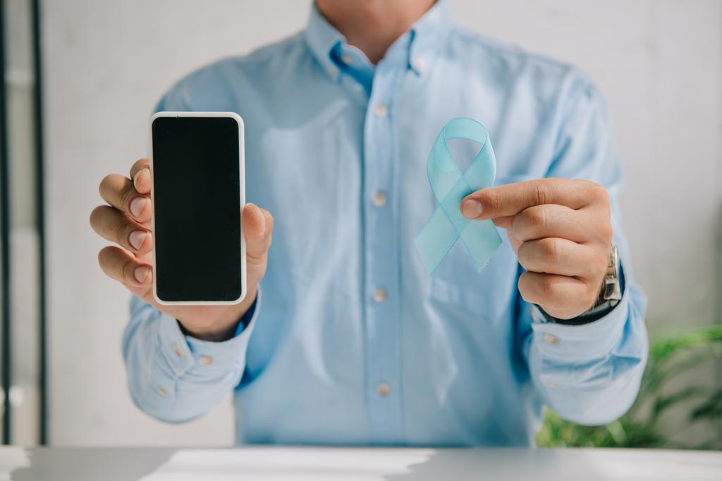 částečný pohled na muže držícího modrou informační stuhu a smartphone s prázdnou obrazovkou - Fotografie, Obrázek