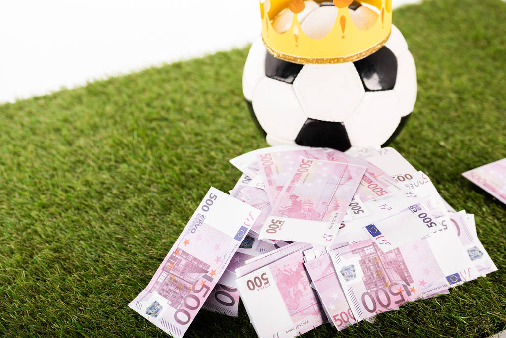 τραπεζογραμμάτια ευρώ κοντά σε μπάλα ποδοσφαίρου με χάρτινη κορώνα σε πράσινο γρασίδι απομονωμένα σε λευκό, έννοια αθλητικών στοιχημάτων - Φωτογραφία, εικόνα