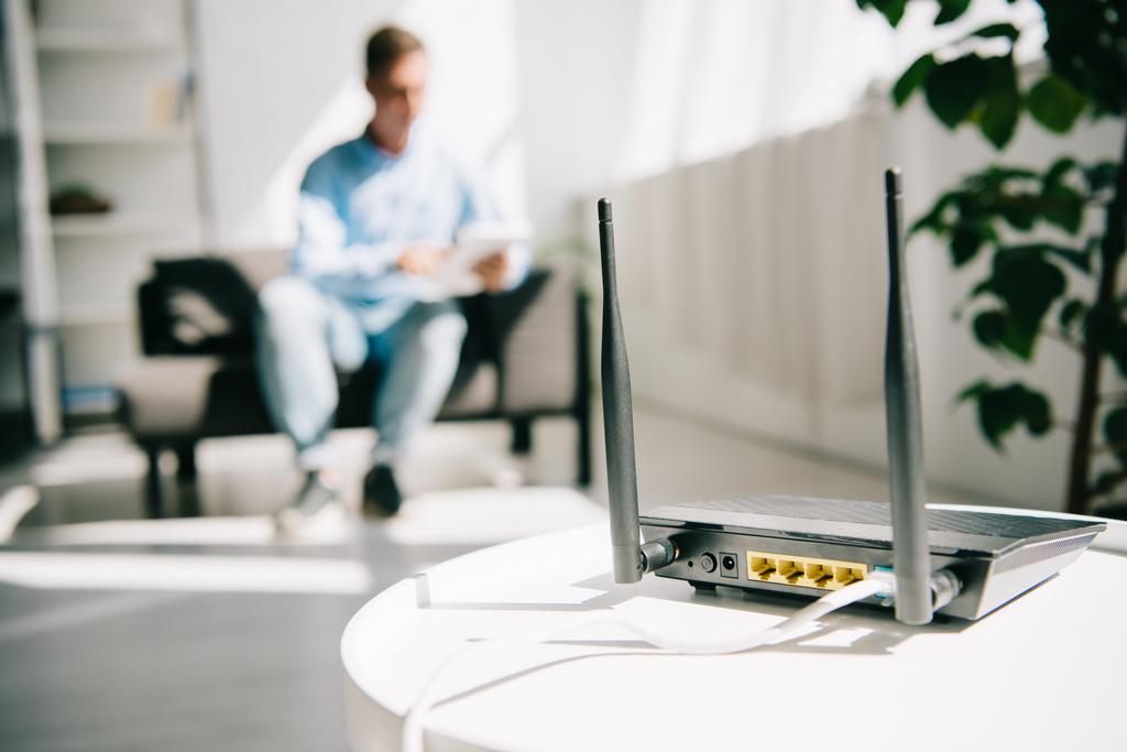 messa a fuoco selettiva di router nero collegato su tavolo bianco e uomo d'affari seduto sul divano
 - Foto, immagini
