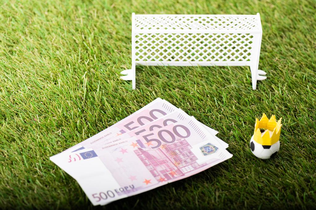 Spielzeug-Fußball mit Papierkrone in der Nähe von Euro-Banknoten und Miniaturtoren, Sportwetten-Konzept - Foto, Bild