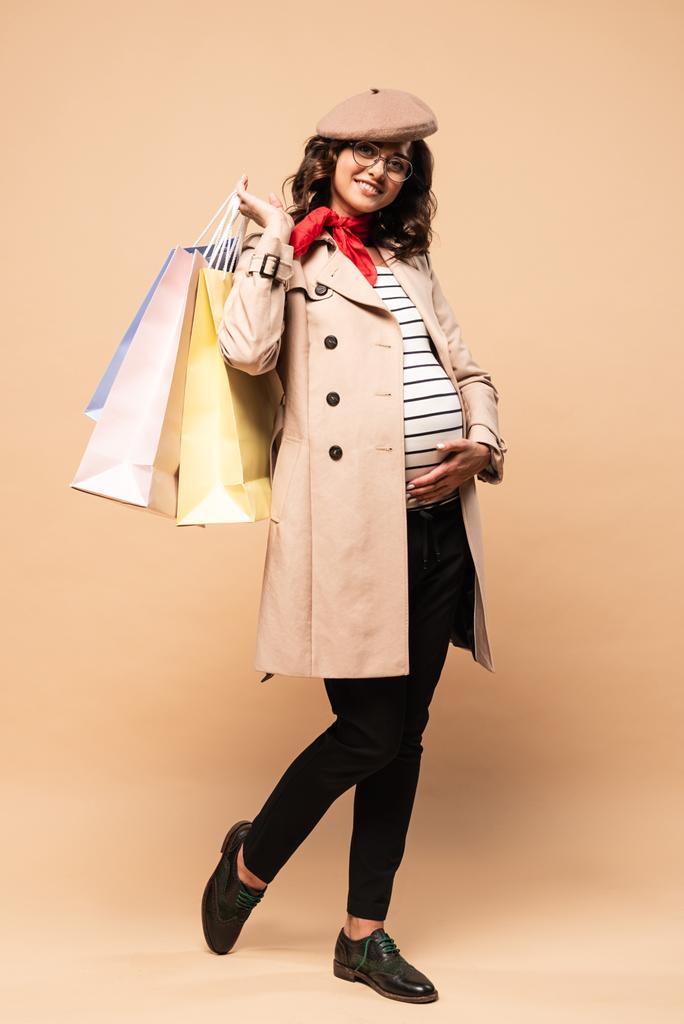 Schwangere Französin im Mantel mit Einkaufstaschen auf beigem Hintergrund  - Foto, Bild