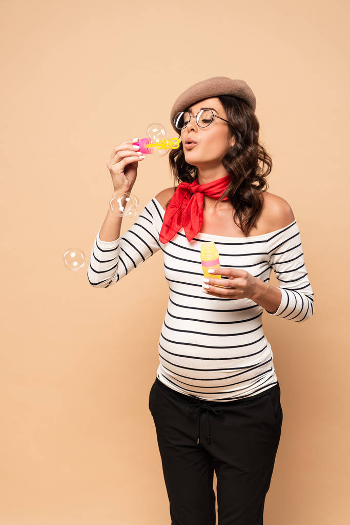 mujer francesa embarazada en boina soplando burbujas de jabón sobre fondo beige
  - Foto, imagen