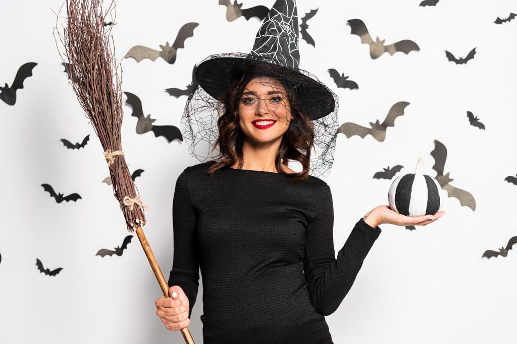 έγκυος γυναίκα σε καπέλο μάγισσα κρατώντας σκούπα και κολοκύθα στο Halloween - Φωτογραφία, εικόνα