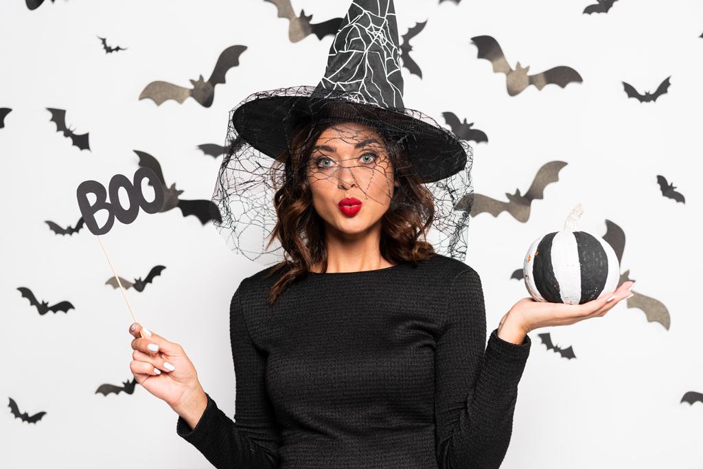wstrząśnięta kobieta w kapeluszu czarownicy trzymając kij z literami boo i dyni w Halloween - Zdjęcie, obraz