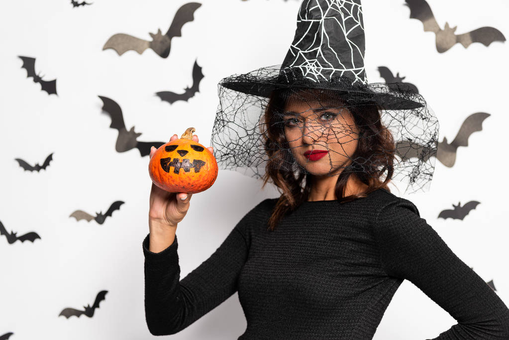 attraktive Frau mit Hexenhut, die zu Halloween einen Kürbis hält - Foto, Bild