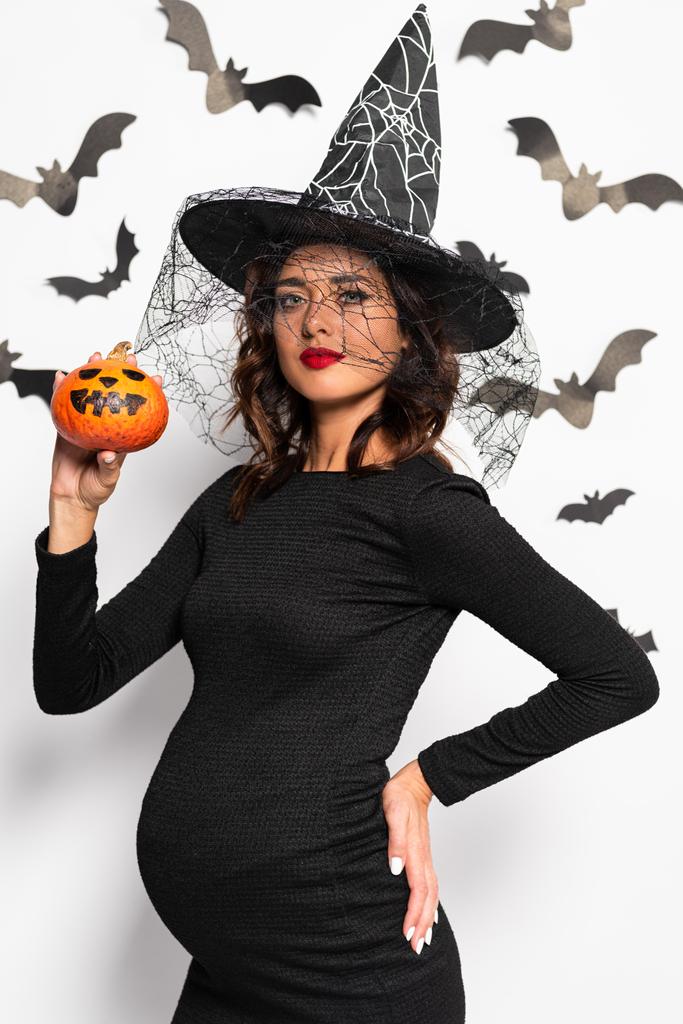 mujer embarazada con sombrero de bruja sosteniendo calabaza en Halloween
 - Foto, imagen