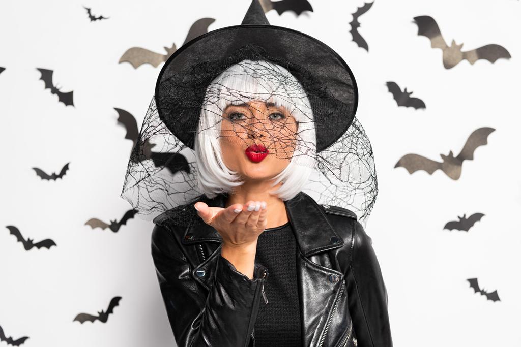 привлекательная женщина в шляпе ведьмы и парик дует поцелуй в Хэллоуин
 - Фото, изображение