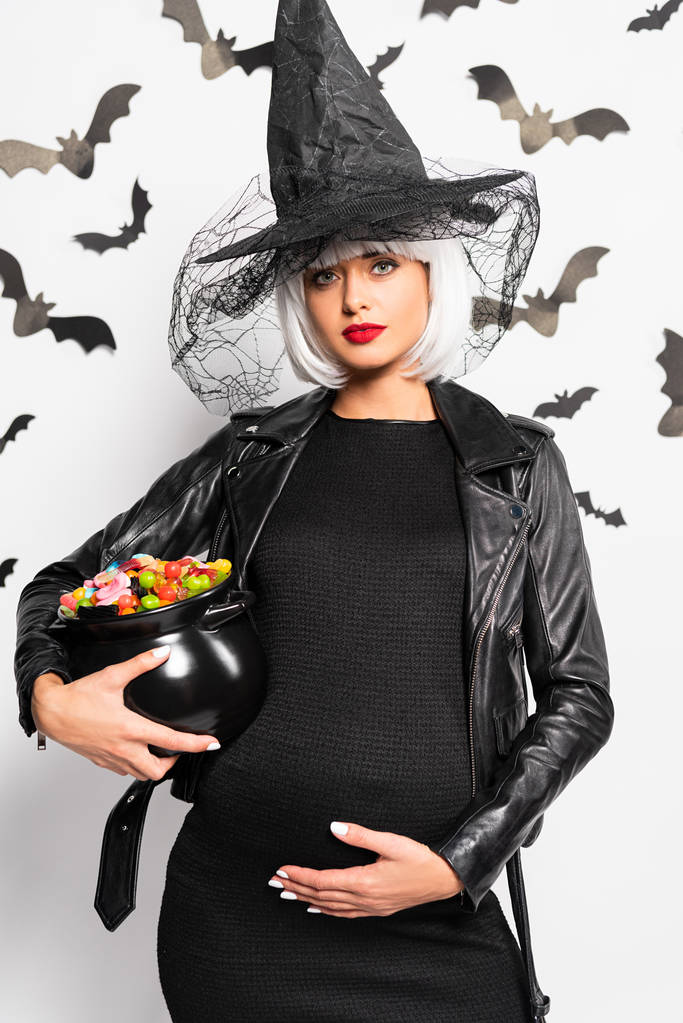 těhotná žena v čarodějnice klobouk a paruka držení pot s bonbóny v halloween - Fotografie, Obrázek