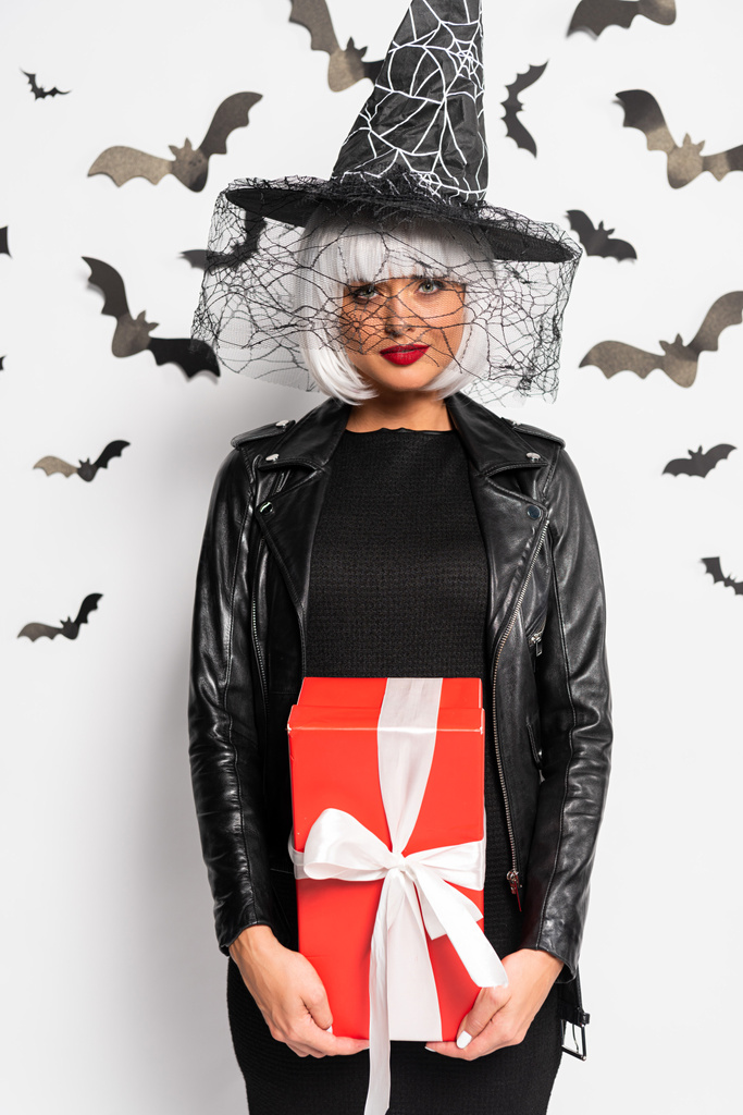 mulher atraente em chapéu de bruxa e peruca segurando presente no Halloween
 - Foto, Imagem