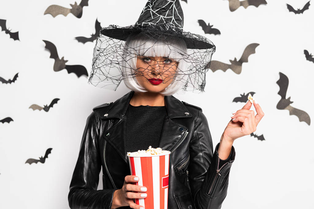 mulher atraente em chapéu de bruxa e peruca segurando pipocas no Halloween
 - Foto, Imagem
