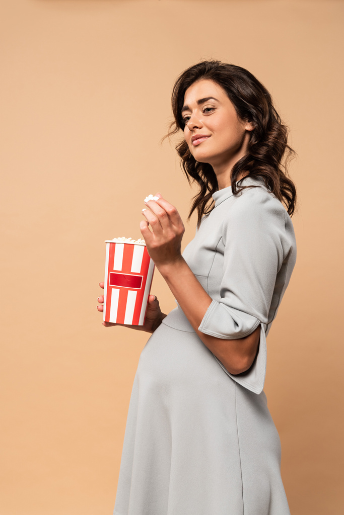 pregnant woman in grey dress holding popcorn on beige background  - Photo, Image
