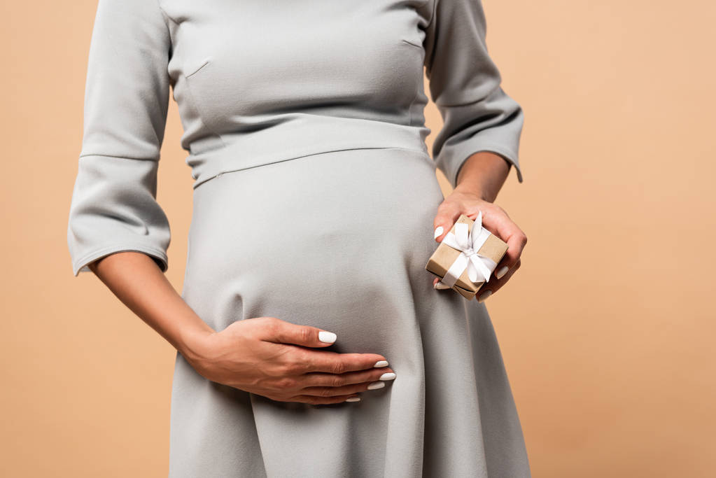 vista ritagliata della donna incinta in abito grigio con regalo su sfondo beige
  - Foto, immagini