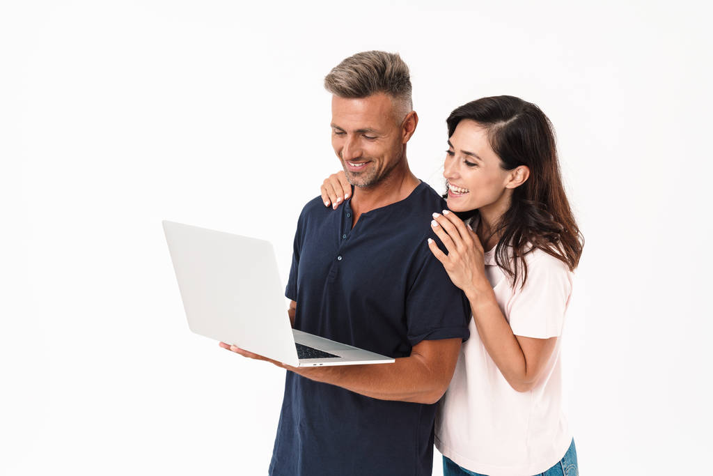 Ευχάριστο θετικό ενήλικα ζευγάρι που απομονώνεται πάνω από λευκό τοίχο φόντο χρησιμοποιώντας φορητό υπολογιστή. - Φωτογραφία, εικόνα