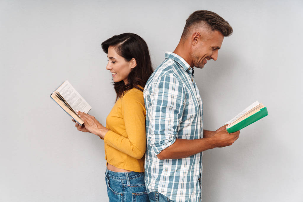 Ευτυχισμένο χαμόγελο ενήλικο ζευγάρι απομονώνεται πάνω από γκρι τοίχο διαβάζοντας βιβλία. - Φωτογραφία, εικόνα