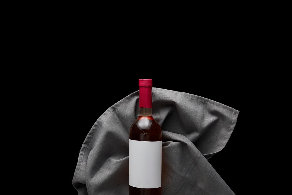vista superior de la botella de vino rosa con etiqueta blanca en blanco en servilleta gris aislada en negro
 - Foto, Imagen