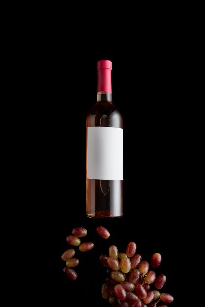 vista superior de la botella con vino rosa y etiqueta blanca en blanco cerca de la uva aislada en negro
 - Foto, imagen