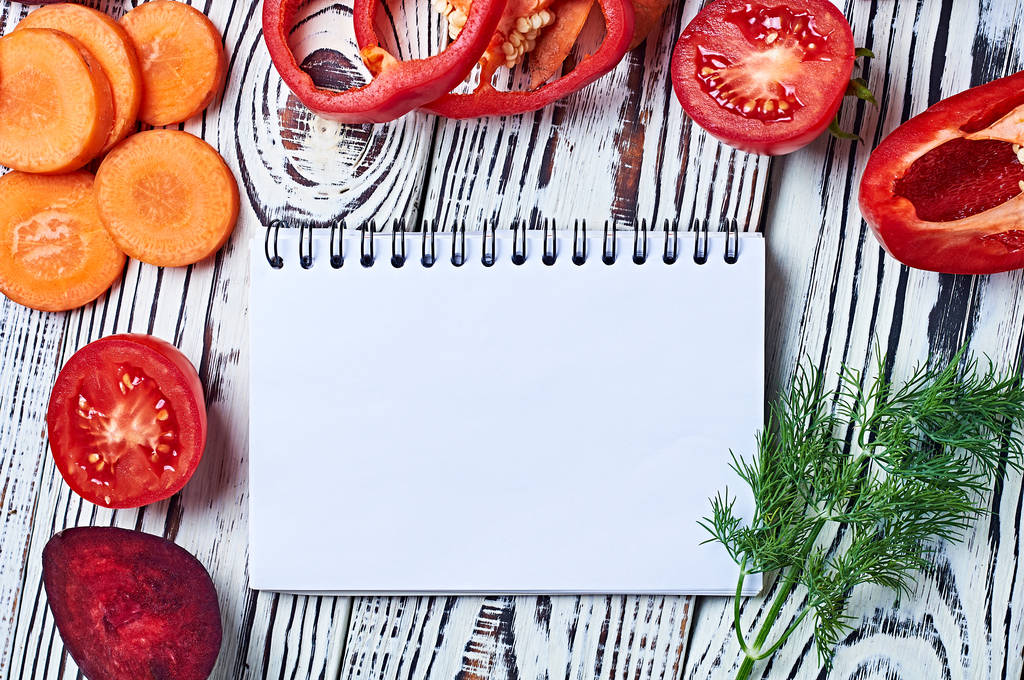Boş kâğıt not defterinin yanında farklı taze, olgun sebzeler mutfaktaki eski, beyaz ahşap masa üzerinde yatar. Sağlıklı gıda konsepti. Mesaj için yer var. Üst görünüm - Fotoğraf, Görsel